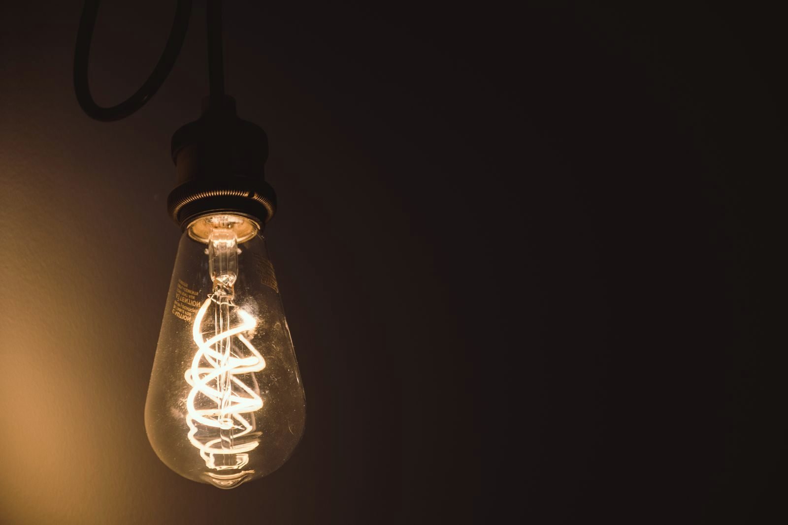 Filament bulb glowing warm against a dark wall