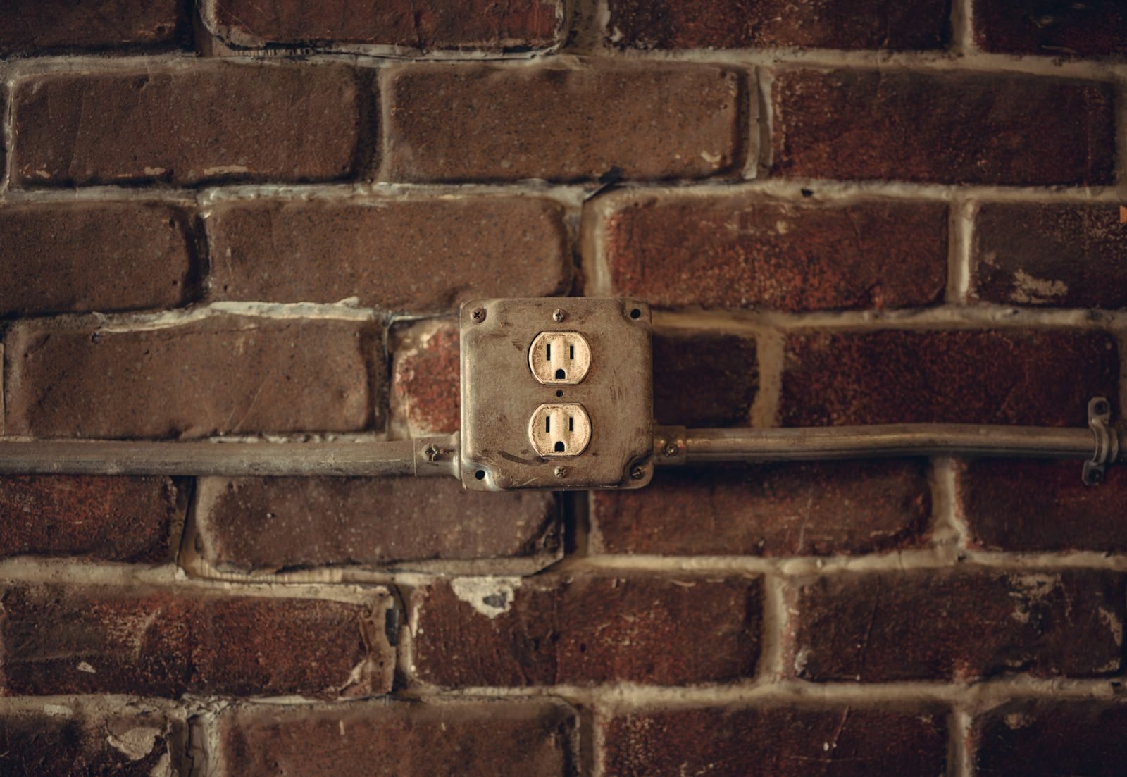 Aged duplex outlet in a galvanized box with conduit on an old brick wall
